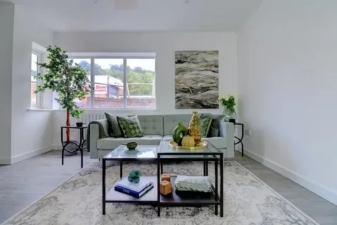 A living room with white walls and ceiling and containing a white sofa with a glass-topped coffee table in front of it